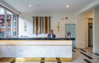 A reception desk with a marble counter, a person standing behind it, and a striped curtain in the background.