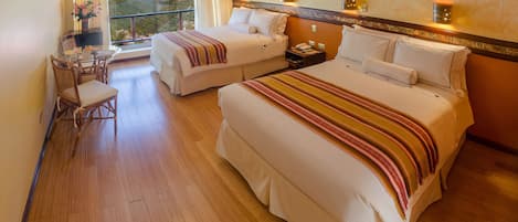 Habitación de hotel con dos camas, un escritorio con silla, televisión y vistas a la montaña.