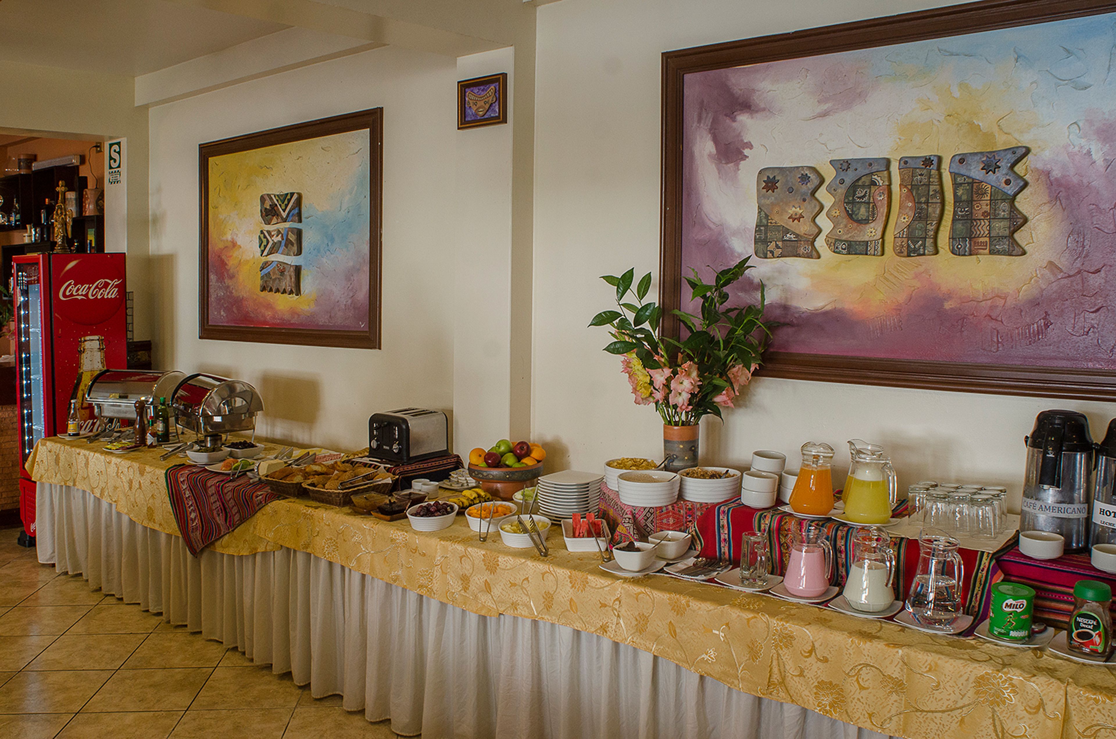 Une table de buffet garnie de divers plats et boissons, un réfrigérateur à Coca-Cola et deux œuvres d’art encadrées accrochées au mur.