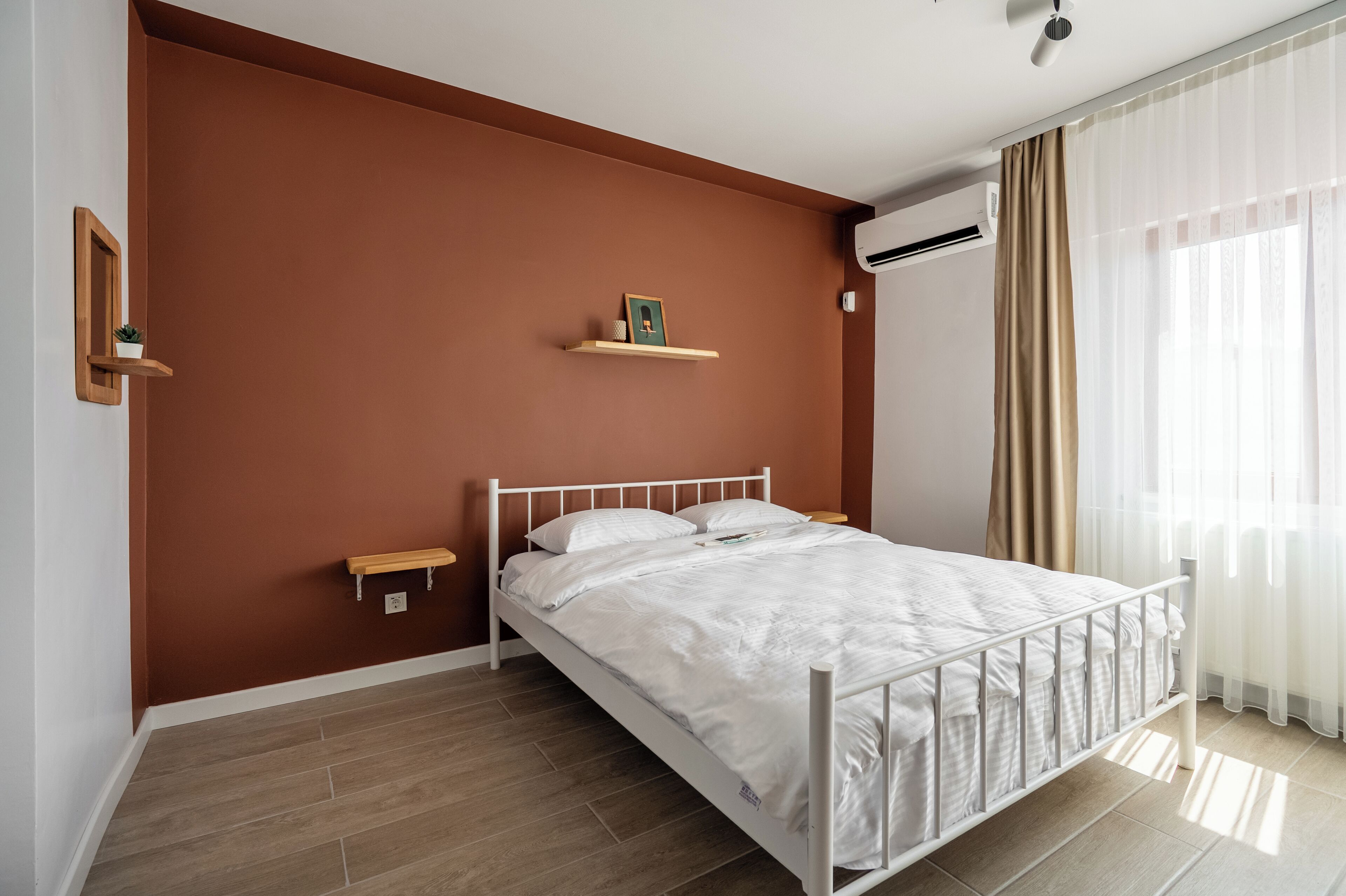 Un dormitorio con cama blanca, paredes marrones y ventana con cortinas traslúcidas.