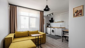 En kompakt opholdsstue med sofa, lille tekøkken og spisebord.