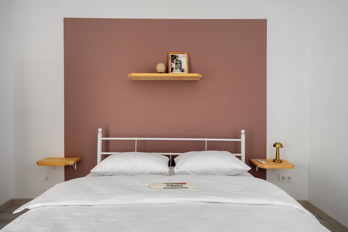 A bed with white bedding, a wooden headboard, two nightstands with lamps, and a shelf above the bed.