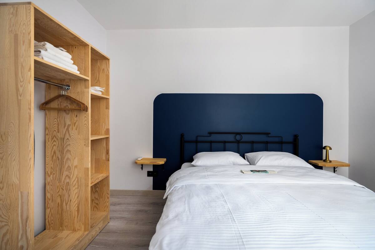 A bedroom with a bed, wooden wardrobe, and bedside tables.