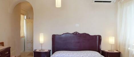 A bedroom with a large bed, two bedside tables, a wardrobe, and a hanging light fixture.