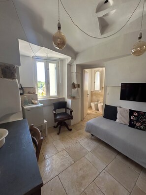A compact living space with a kitchenette, a dining area, a sofa, a TV, and a bathroom. - Masseria Pelosella B&B (Fasano)