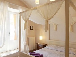 Una habitación con una cama con dosel, una mesita de noche, una lámpara y una ventana con cortinas.