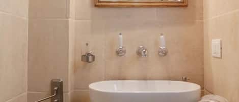 Un baño con un lavamanos blanco, un espejo encima y un perchero a la izquierda.