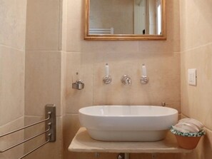 Ein Badezimmer mit einem weißen Waschbecken, einem Spiegel darüber und einem Handtuchhalter links.