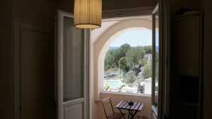 A balcony with a view of a pool and trees, a wooden table and chair, and a hanging light fixture. - Masseria Pelosella B&B (Fasano)