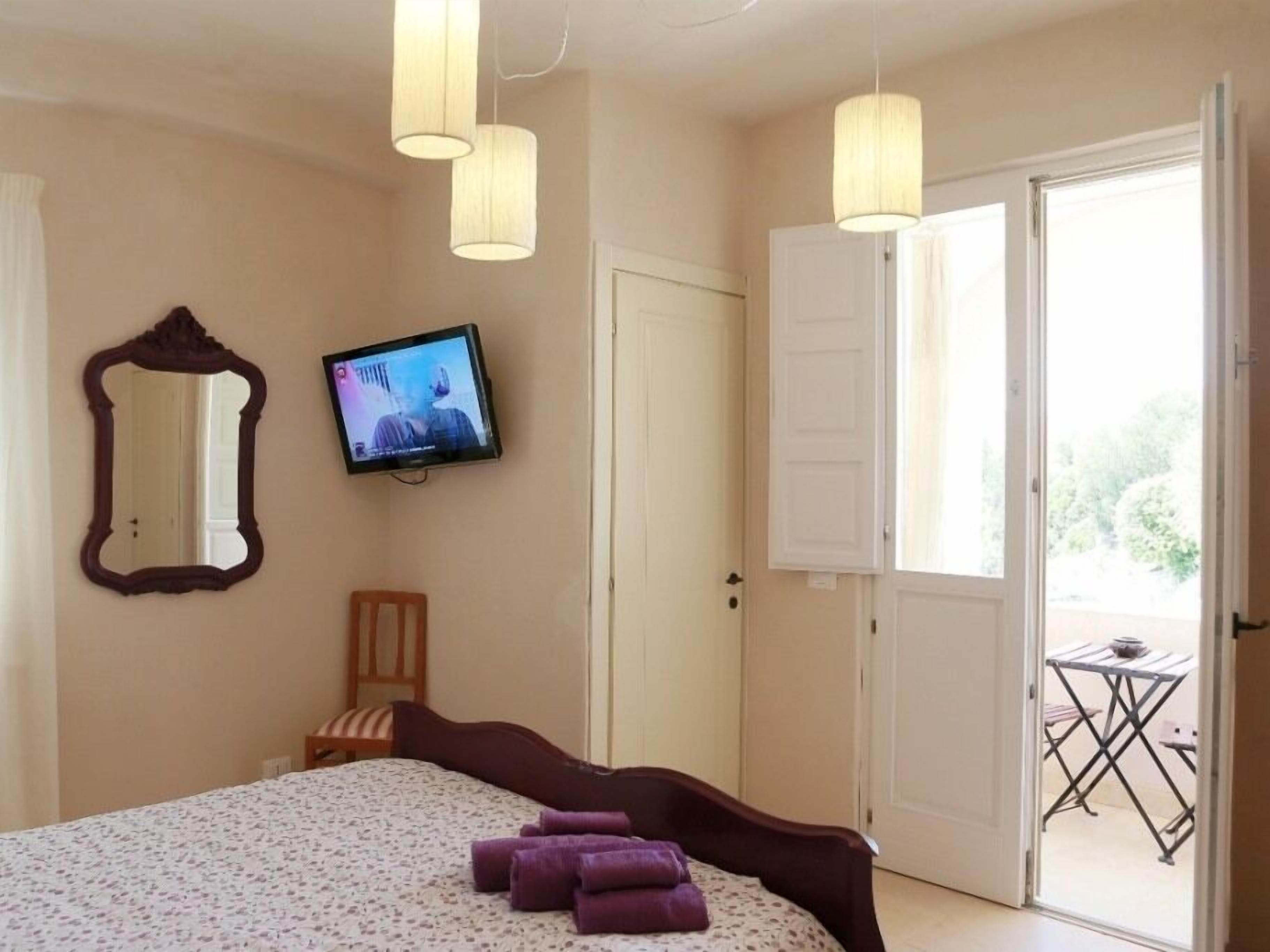 A bedroom with a bed, a television on the wall, a mirror, and a door leading to an outdoor area.