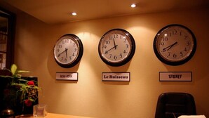 Three clocks on a wall labeled "NEW-YORK," "Le Ruisseau," and "SYDNEY," with a desk and chair in front. - Le Ruisseau (Saint-Mandé)