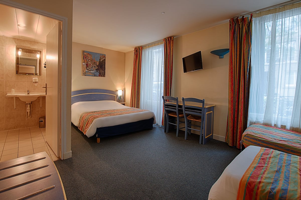 A hotel room with a bed, a desk, a chair, a TV, and a bathroom.