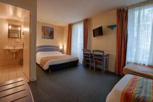 Una habitación de hotel con cama, escritorio, silla, televisor y baño.