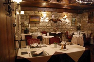 Restaurante com paredes de pedra, vigas de madeira e mesas preparadas para refeições.