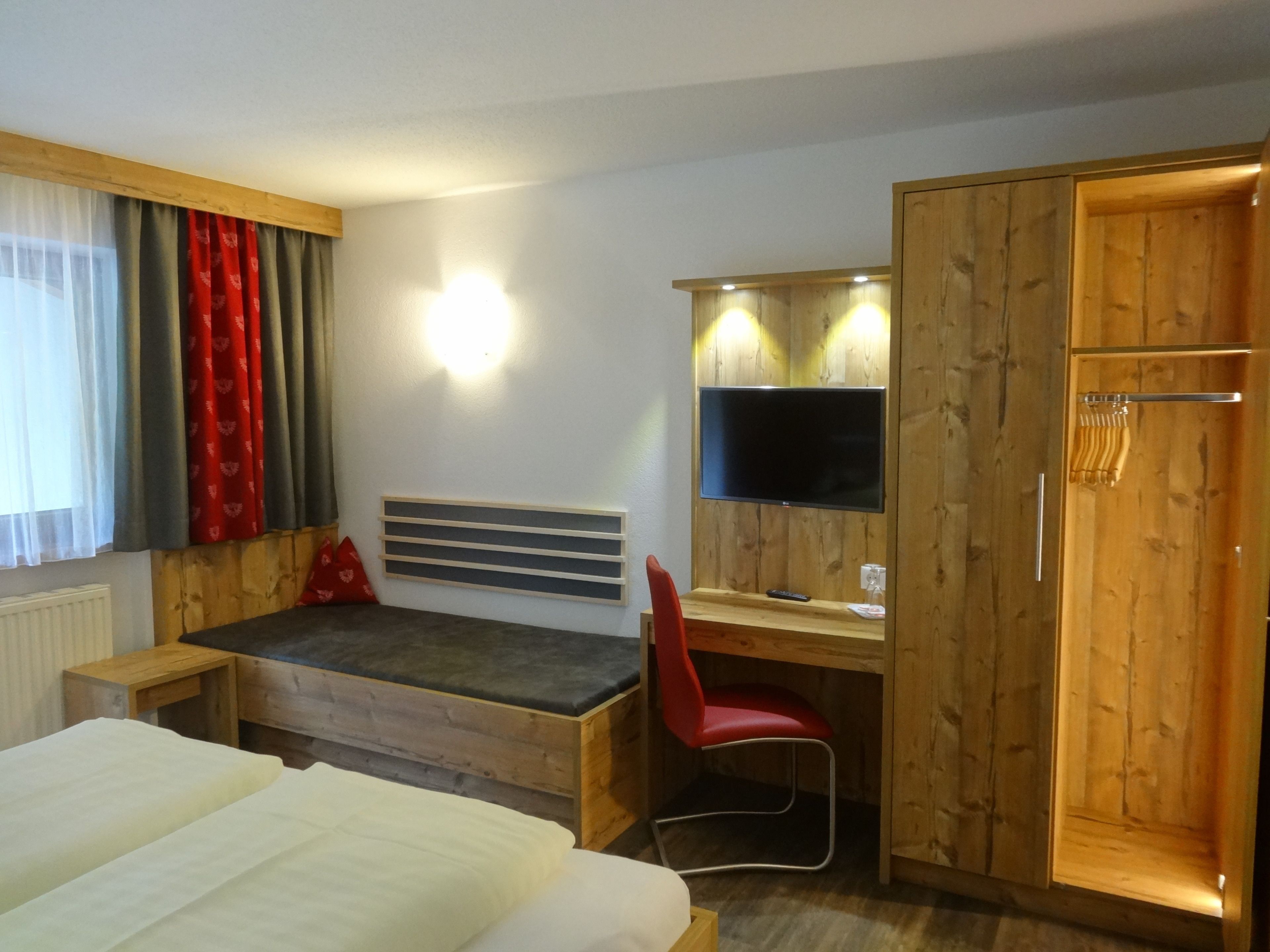 A bedroom with a bed, a desk with a chair, a TV, and a wardrobe.