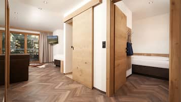 Une chambre d’hôtel moderne avec un plancher en bois, un lit, un téléviseur fixé au mur et une porte coulissante donnant sur une autre pièce.
