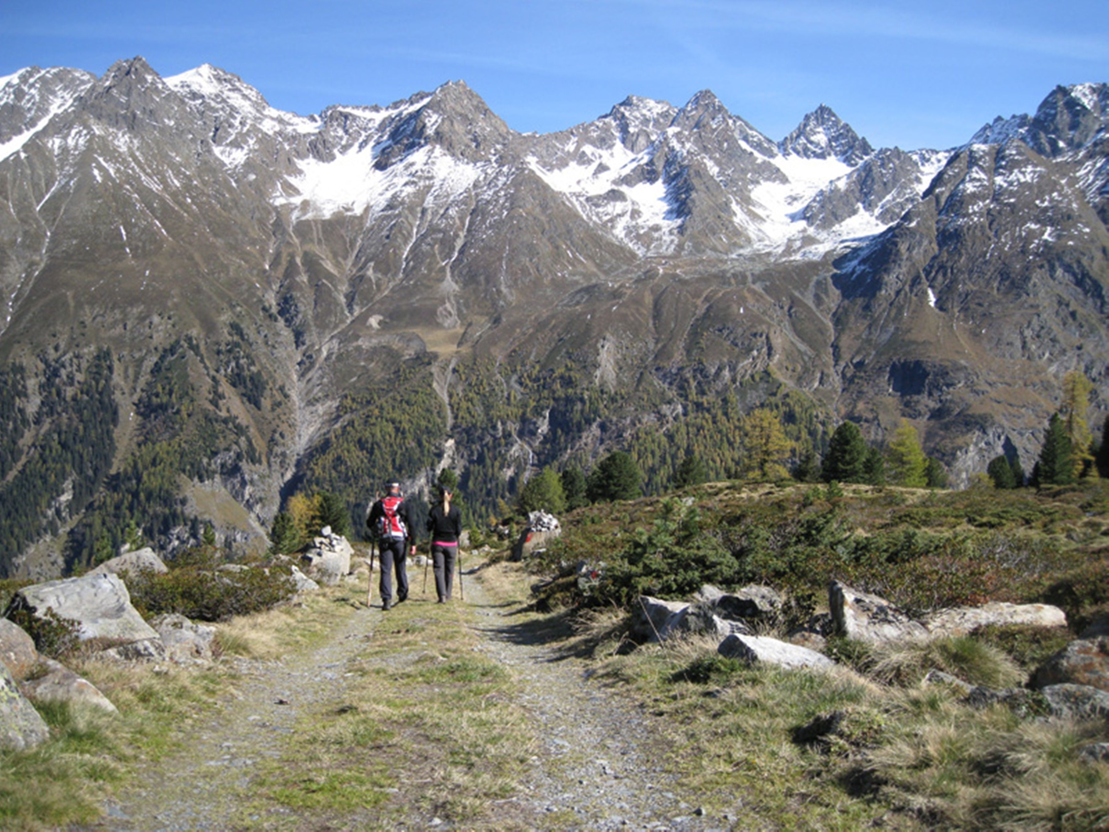 Un sendero de montaña con excursionistas, rodeado de terreno rocoso y picos nevados.