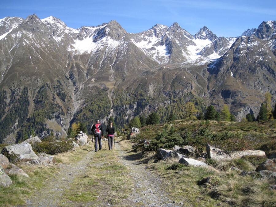 Un sendero de montaña con excursionistas, rodeado de terreno rocoso y picos nevados.