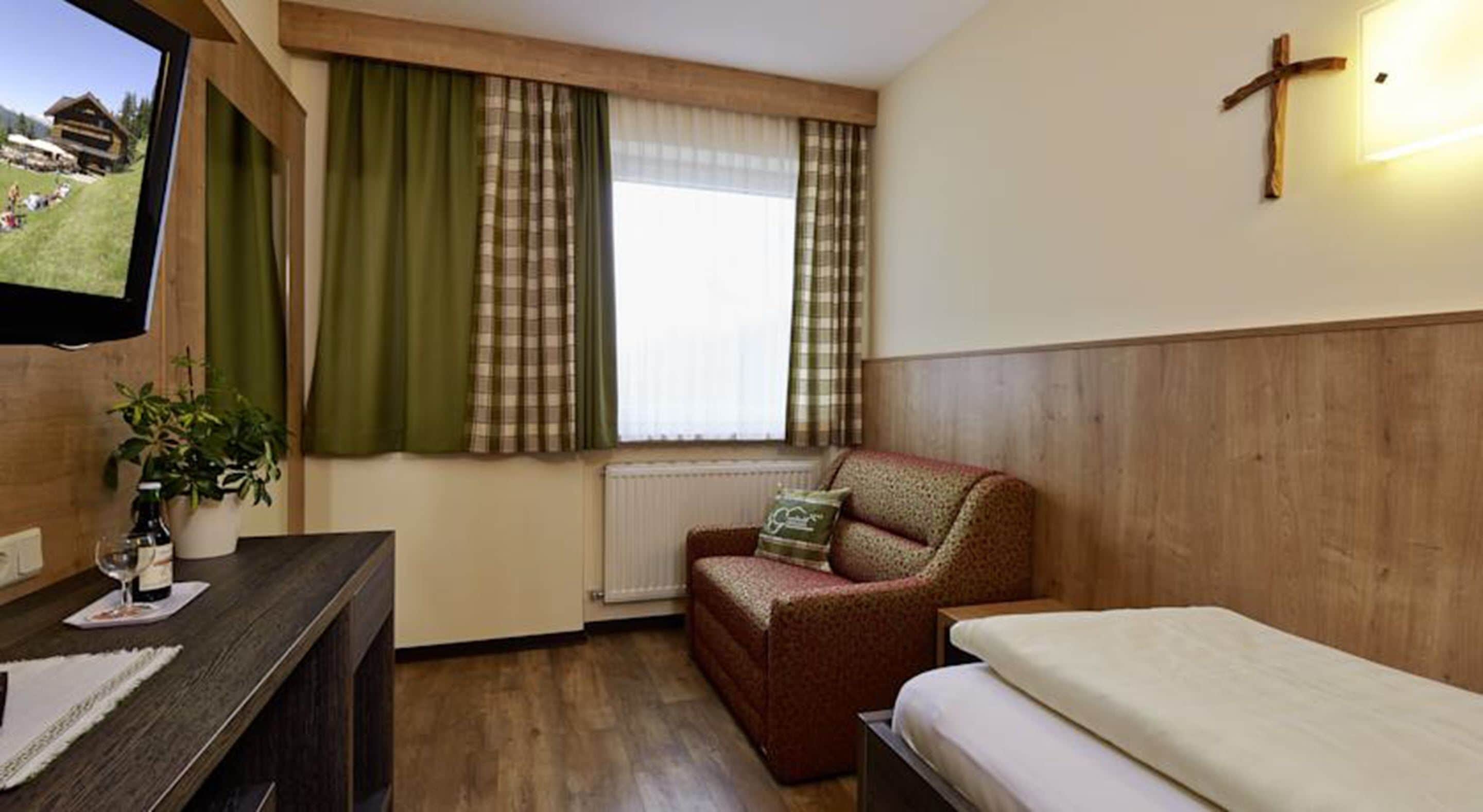 A cozy room with a wooden floor, a bed, a sofa, a TV, and a window with curtains.