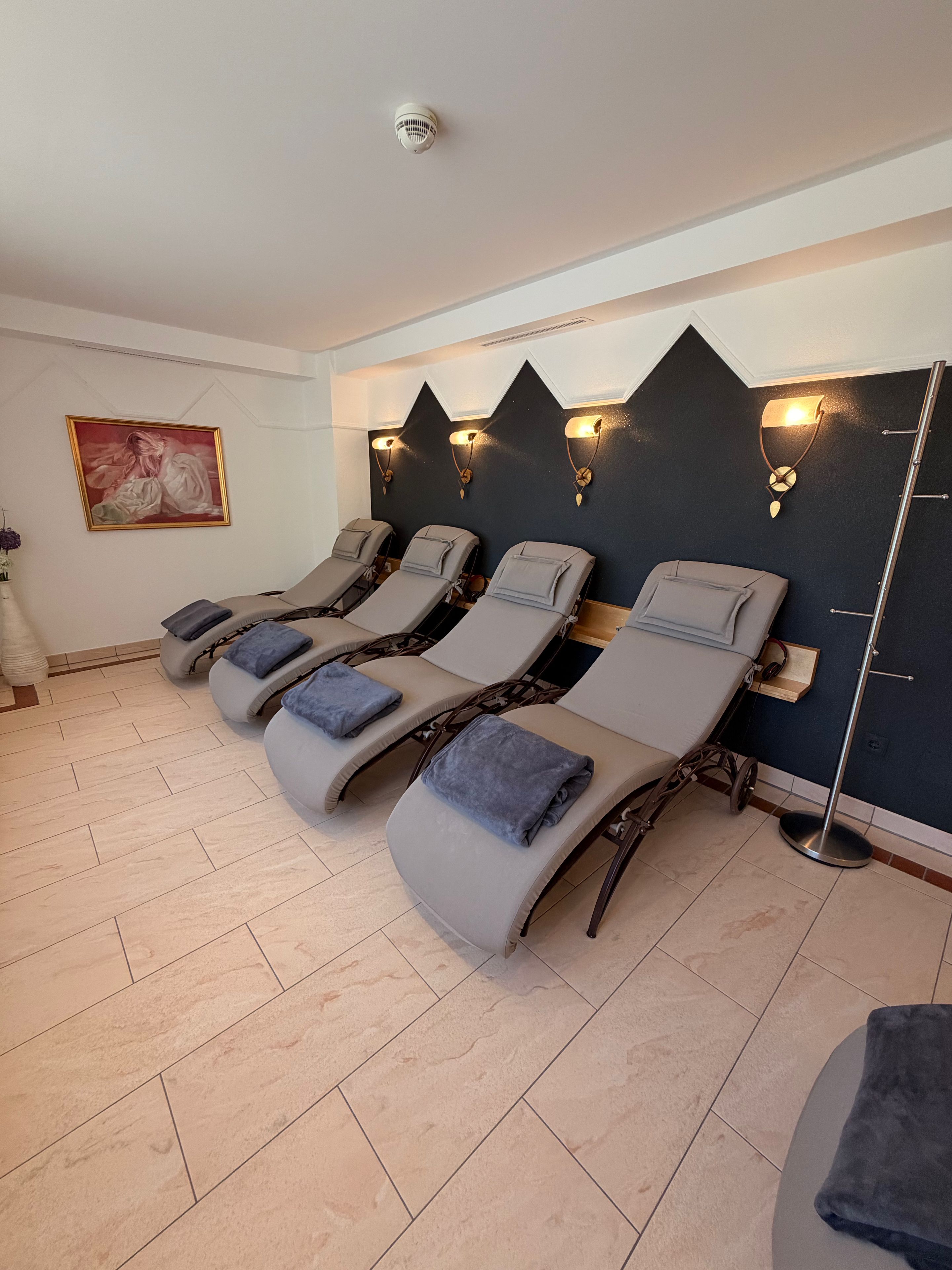 Ein Raum mit vier Liegesesseln, einem an der Wand befestigten Massagestuhl und einem an der Decke montierten Brandmelder.