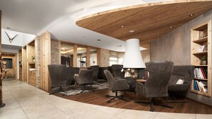 A modern interior with a curved ceiling, grey upholstered chairs, a white lamp, and a bookshelf. - Hotel Gundolf  (Sankt Leonhard im Pitztal)