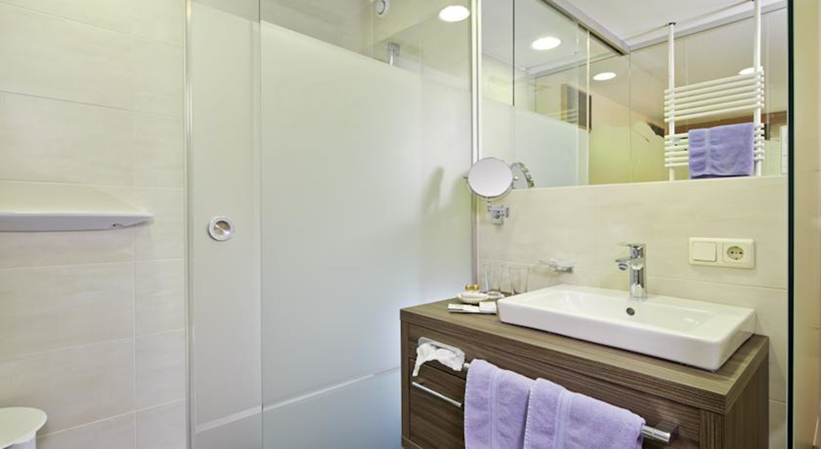 Un baño moderno con cabina de ducha de vidrio, un lavamanos blanco y un mueble de tocador de madera.