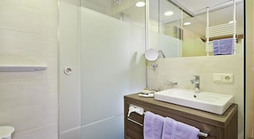 Un baño moderno con cabina de ducha de vidrio, un lavamanos blanco y un mueble de tocador de madera.