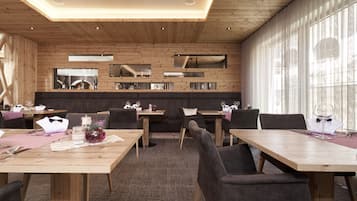 A modern dining area with wooden tables and chairs, a central bar area, and large windows allowing natural light.