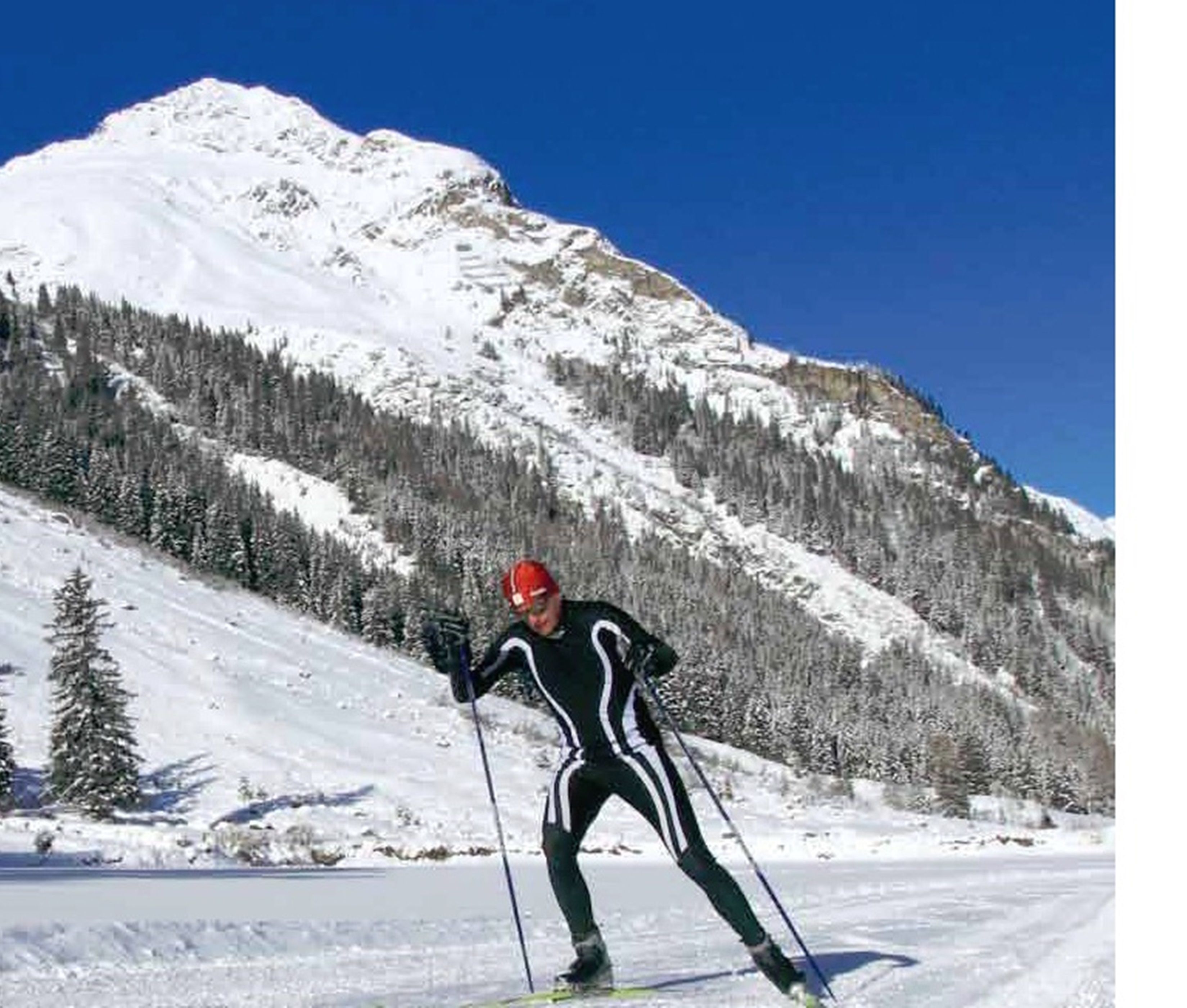 Eine Person langlaufsport begeistert auf einem verschneiten Hang, im Hintergrund ein Berg.