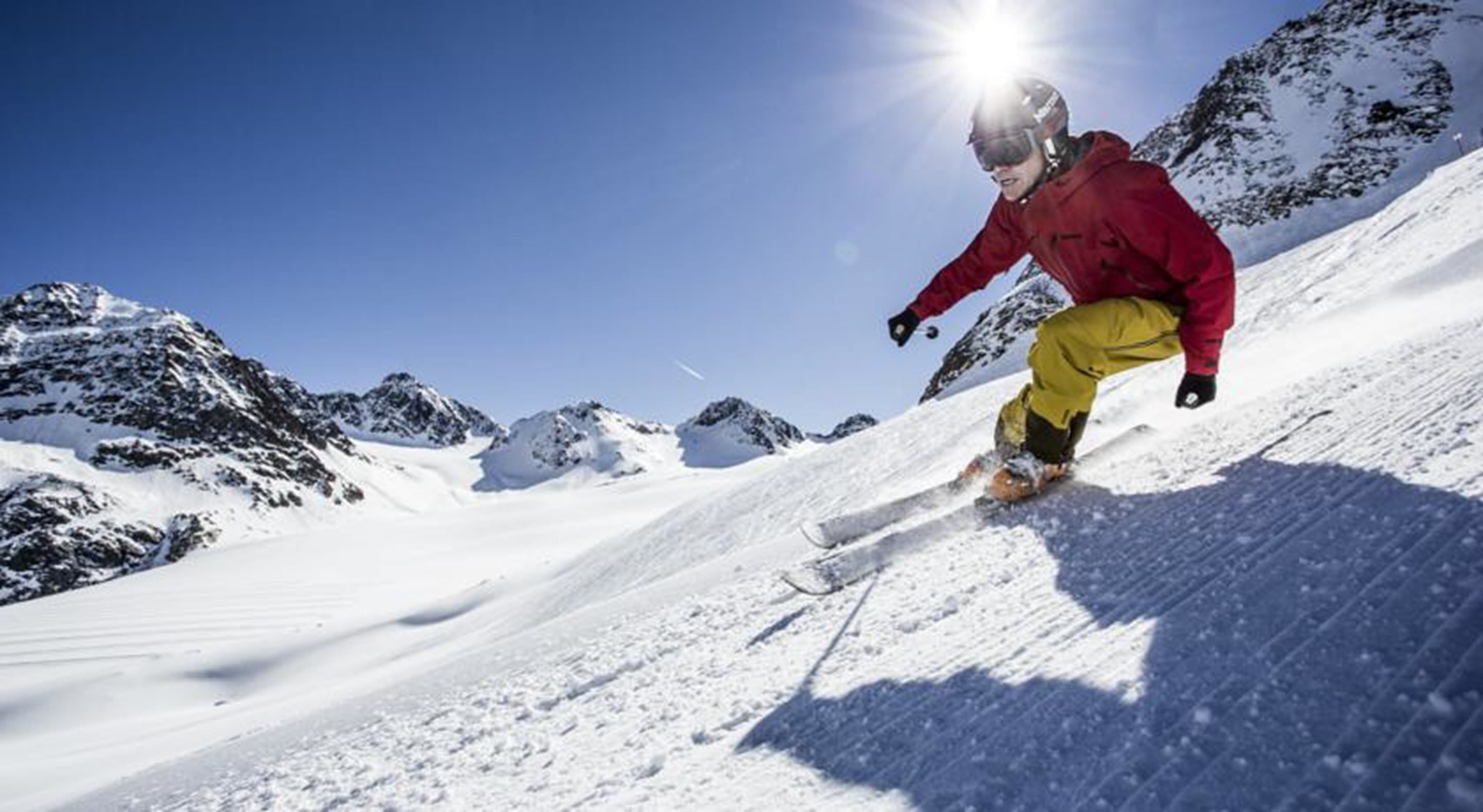 Iemand snowboardt een besneeuwde helling af, met bergen op de achtergrond.