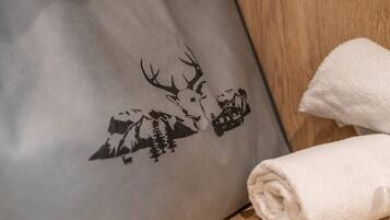Un coussin orné d’un motif représentant un cerf et un chalet de montagne, une serviette blanche roulée et une surface en bois.