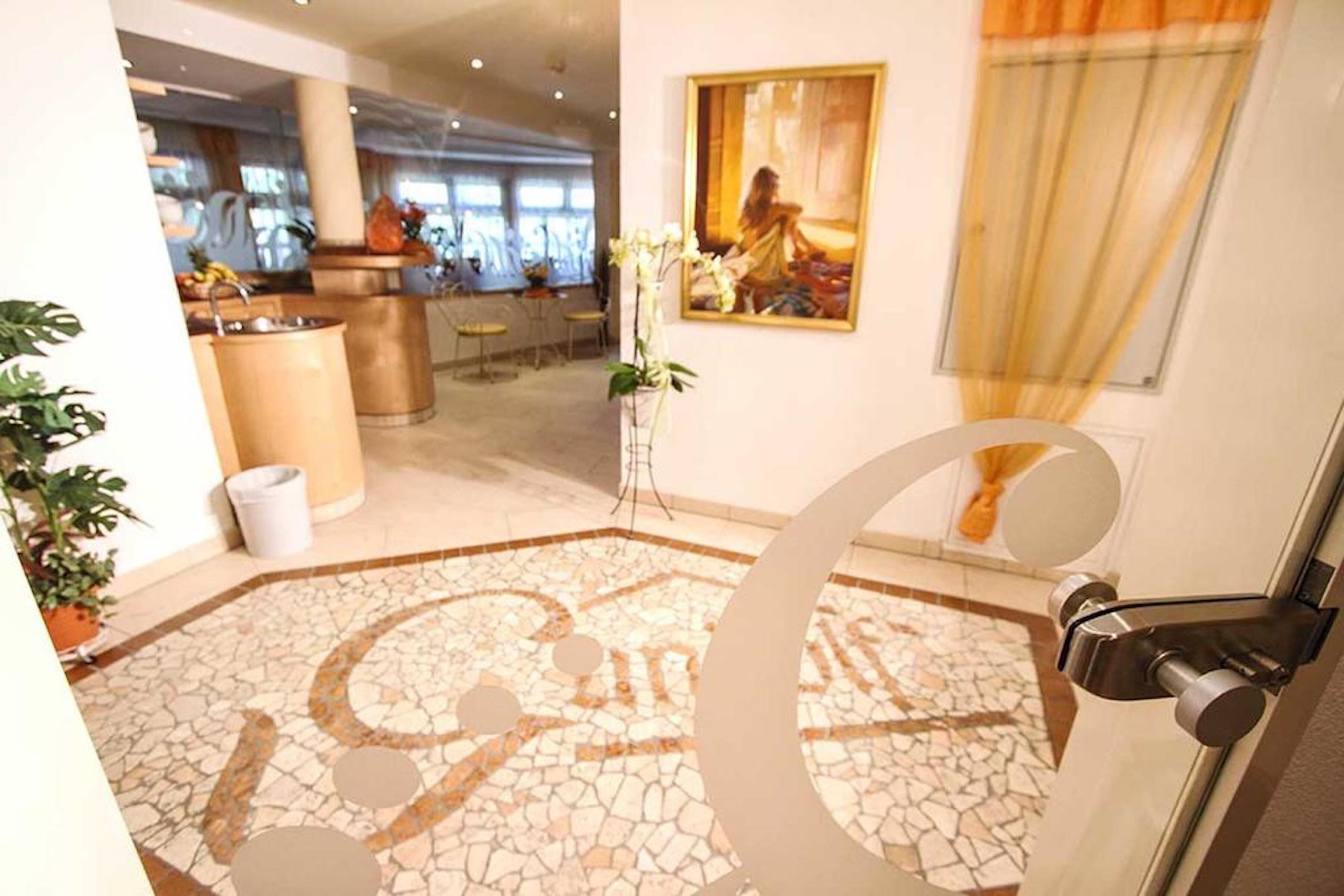 A lobby with a mosaic floor, a large decorative letter 'G', a painting, and a plant.