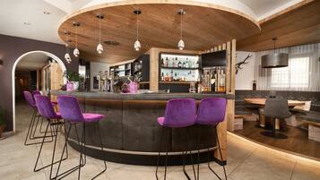 A bar area with a curved wooden counter, purple bar stools, and a variety of bottles on shelves.