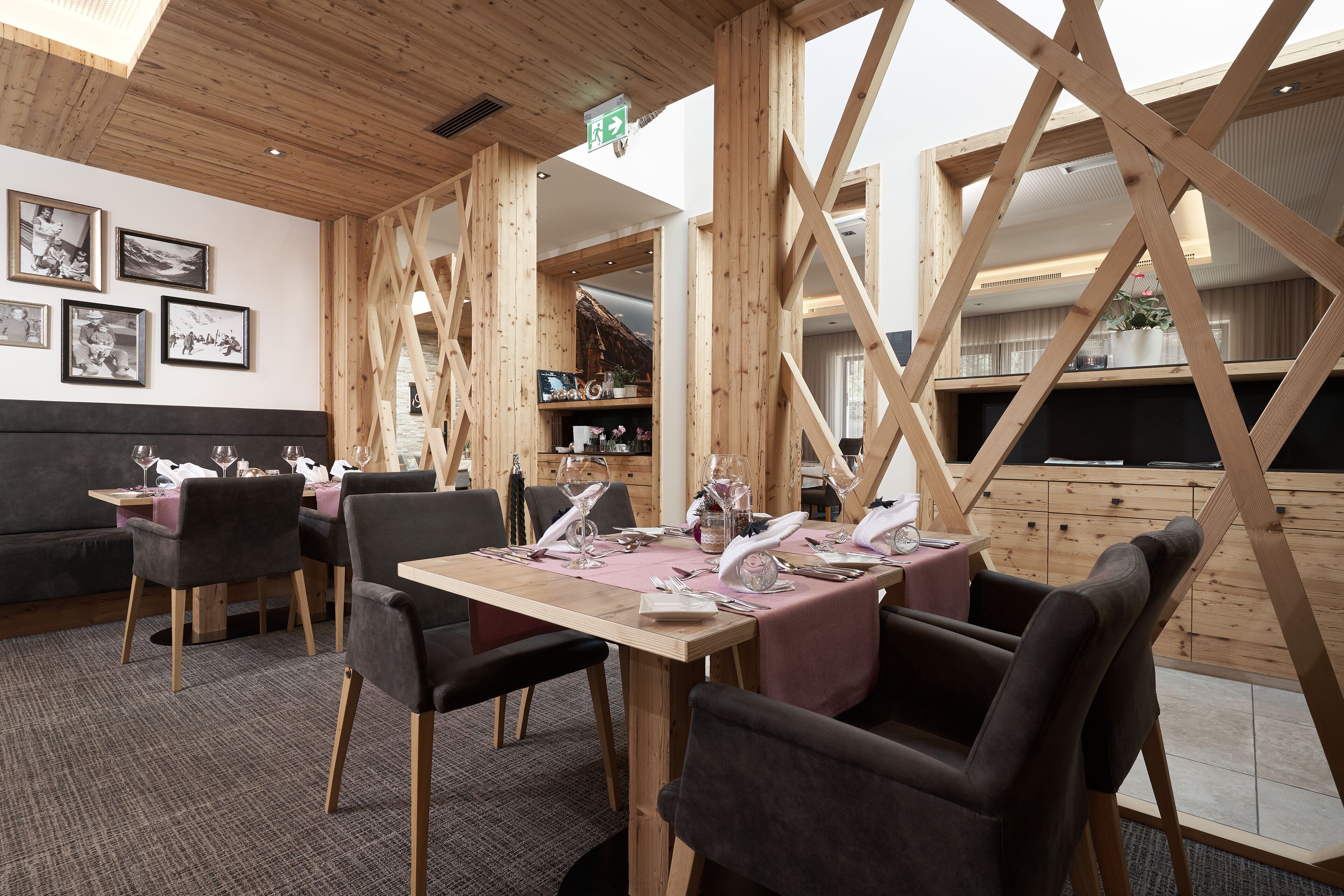Un coin repas agrémenté de poutres en bois, une longue table dressée pour quatre personnes et un canapé en arrière-plan.