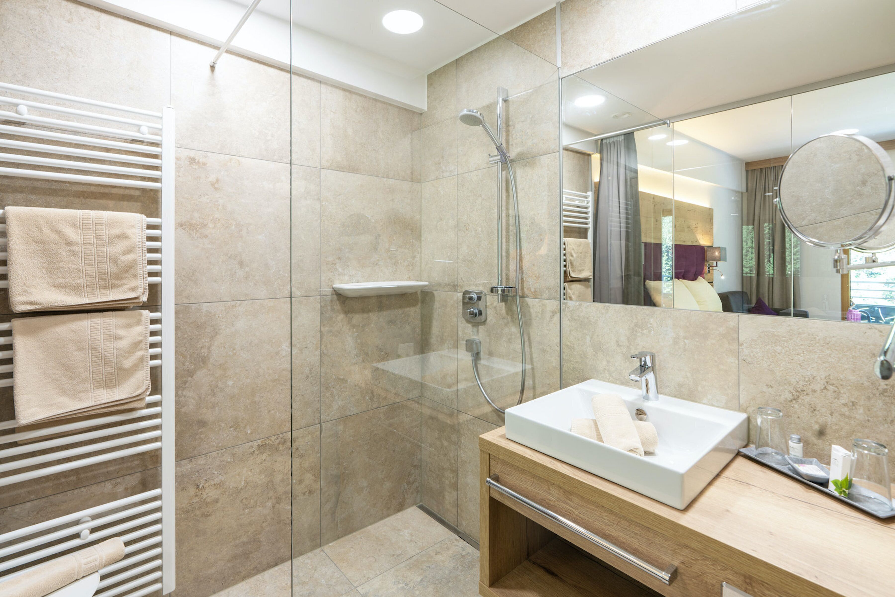 A modern bathroom with a glass-enclosed shower, a wooden vanity with a sink, and a towel rack with multiple towels.