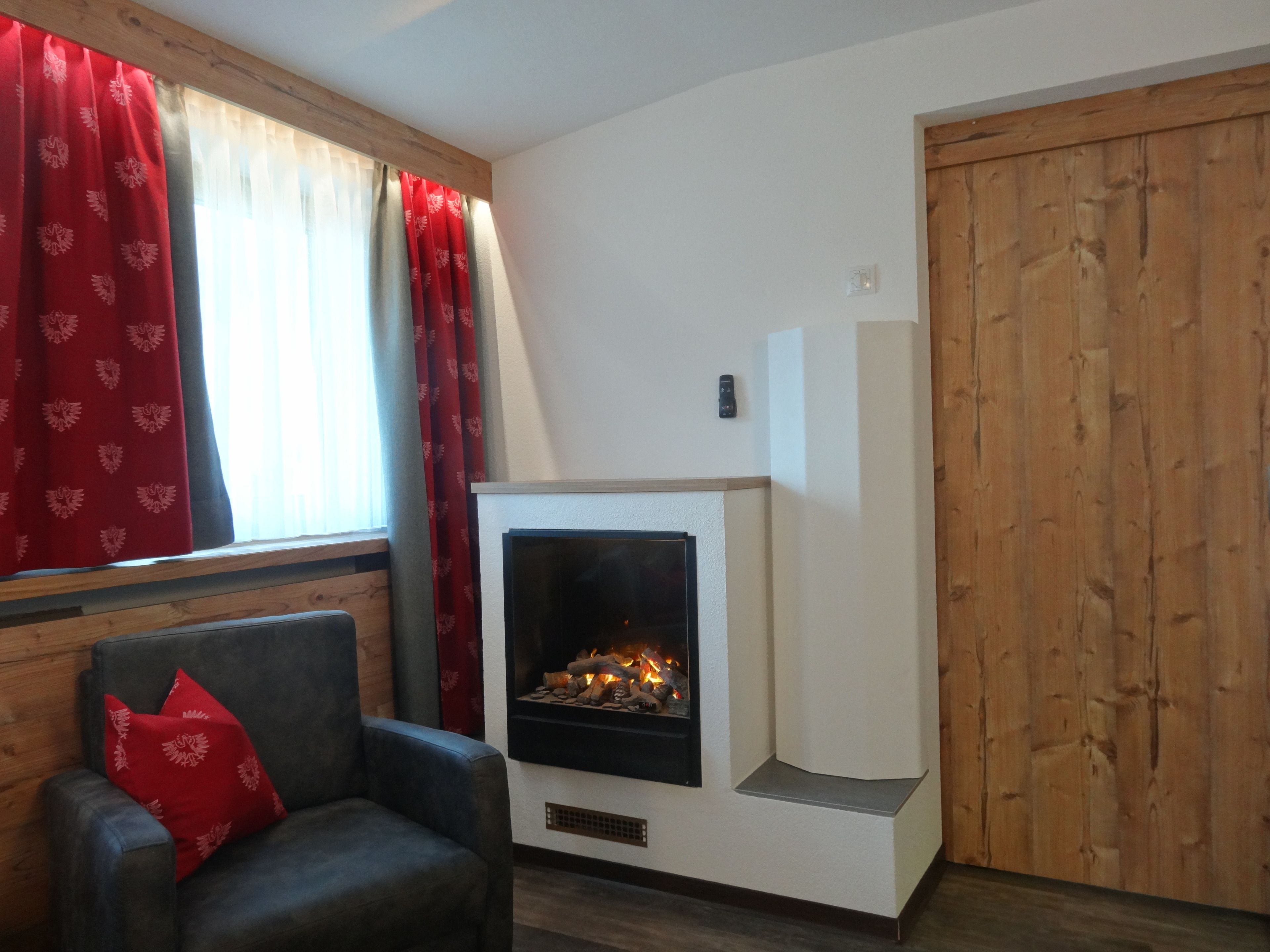 A cozy room with a fireplace, a wooden door, and a window with red curtains.