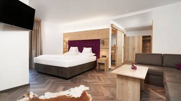 A modern hotel room with a large bed, a sofa, a small table, and a TV.