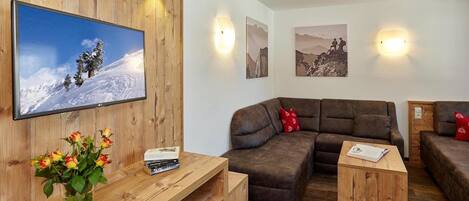 Una sala acogedora con un mueble de televisión de madera, un sofá de cuero marrón y una pequeña mesa de centro de madera.
