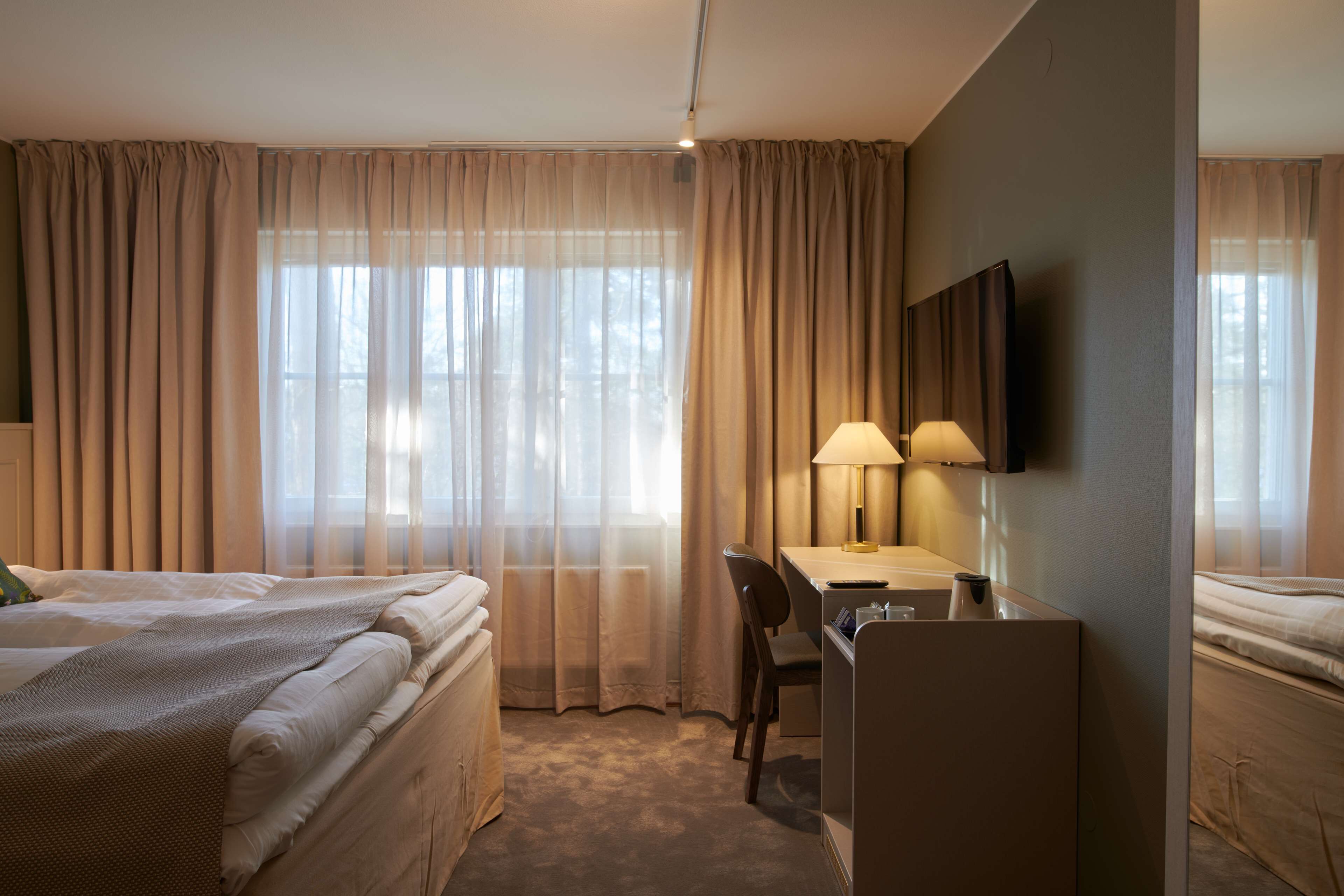 Habitación de hotel con dos camas, un escritorio con silla, un televisor y una lámpara.