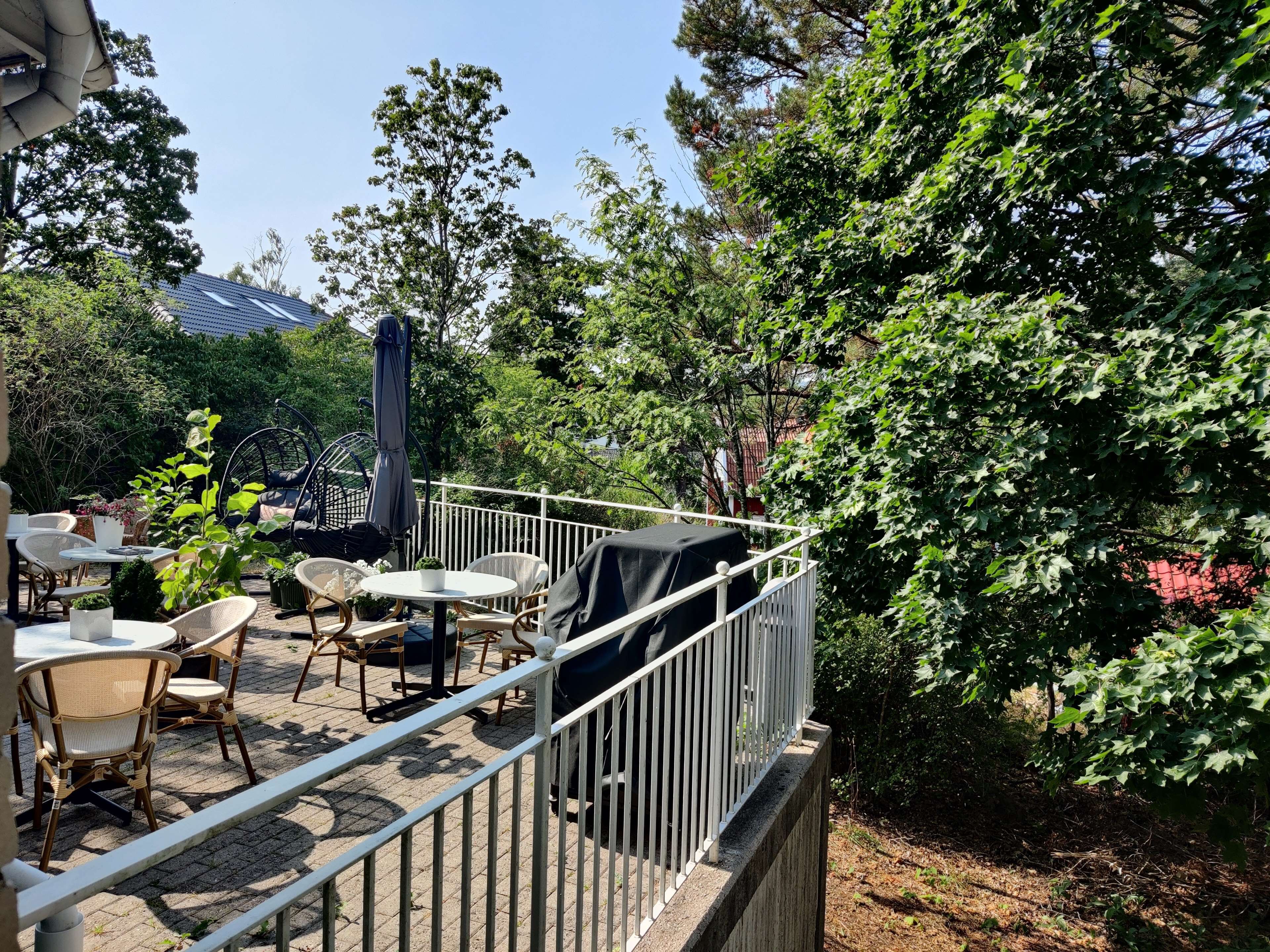 An outdoor patio with wicker furniture, a grill, and a white railing.