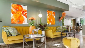 Een moderne woonkamer met een gele bank, een ronde salontafel en kunstwerken aan de wanden.