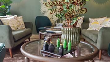 A modern living room with a glass coffee table, green sofas, and a decorative plant.