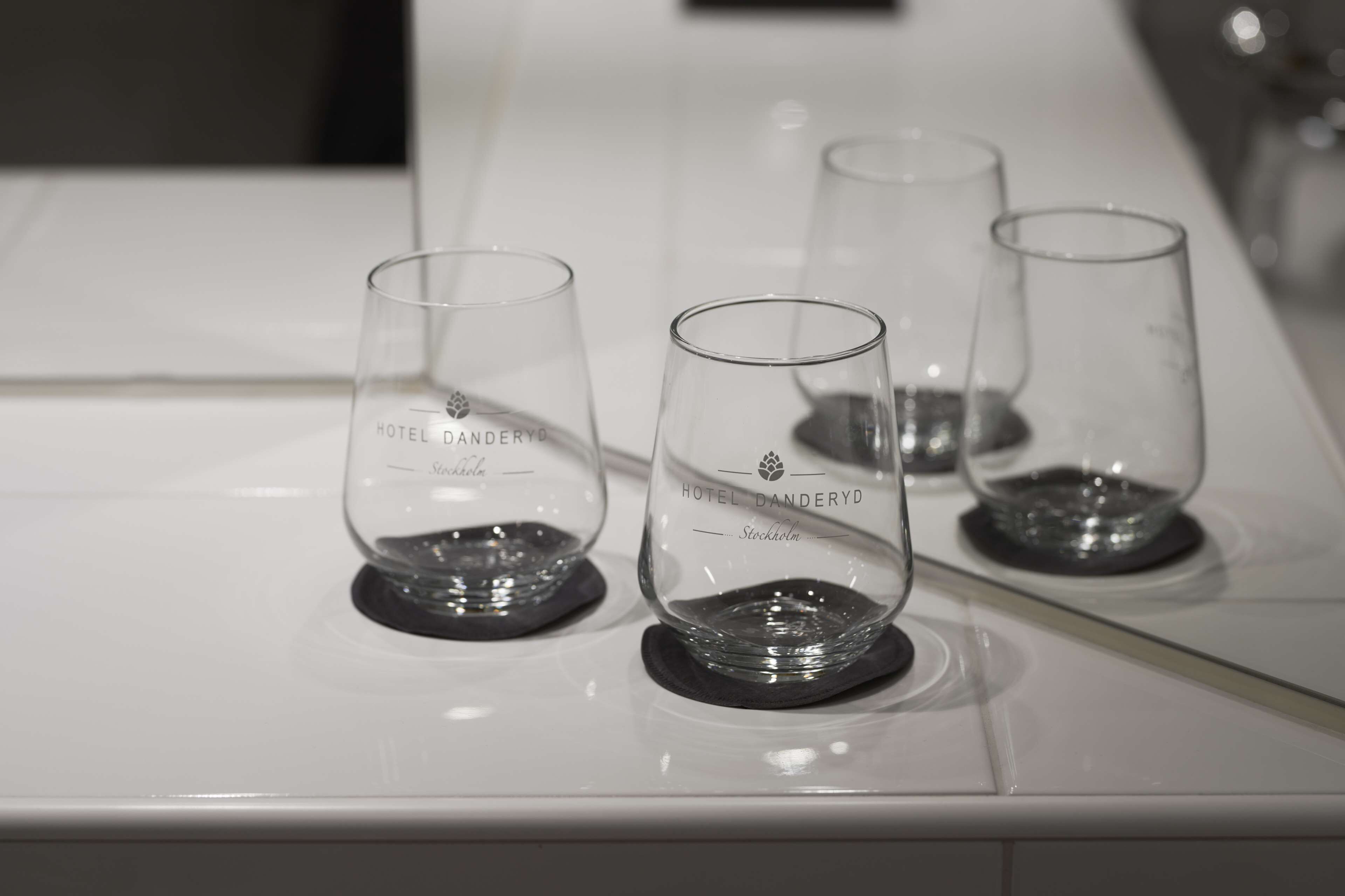 Three empty wine glasses on a white countertop with the text "HOTEL DANDERYD Stockholm" engraved on them.