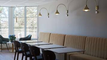 Een moderne eetruimte met een lange bank, meerdere tafels en stoelen.