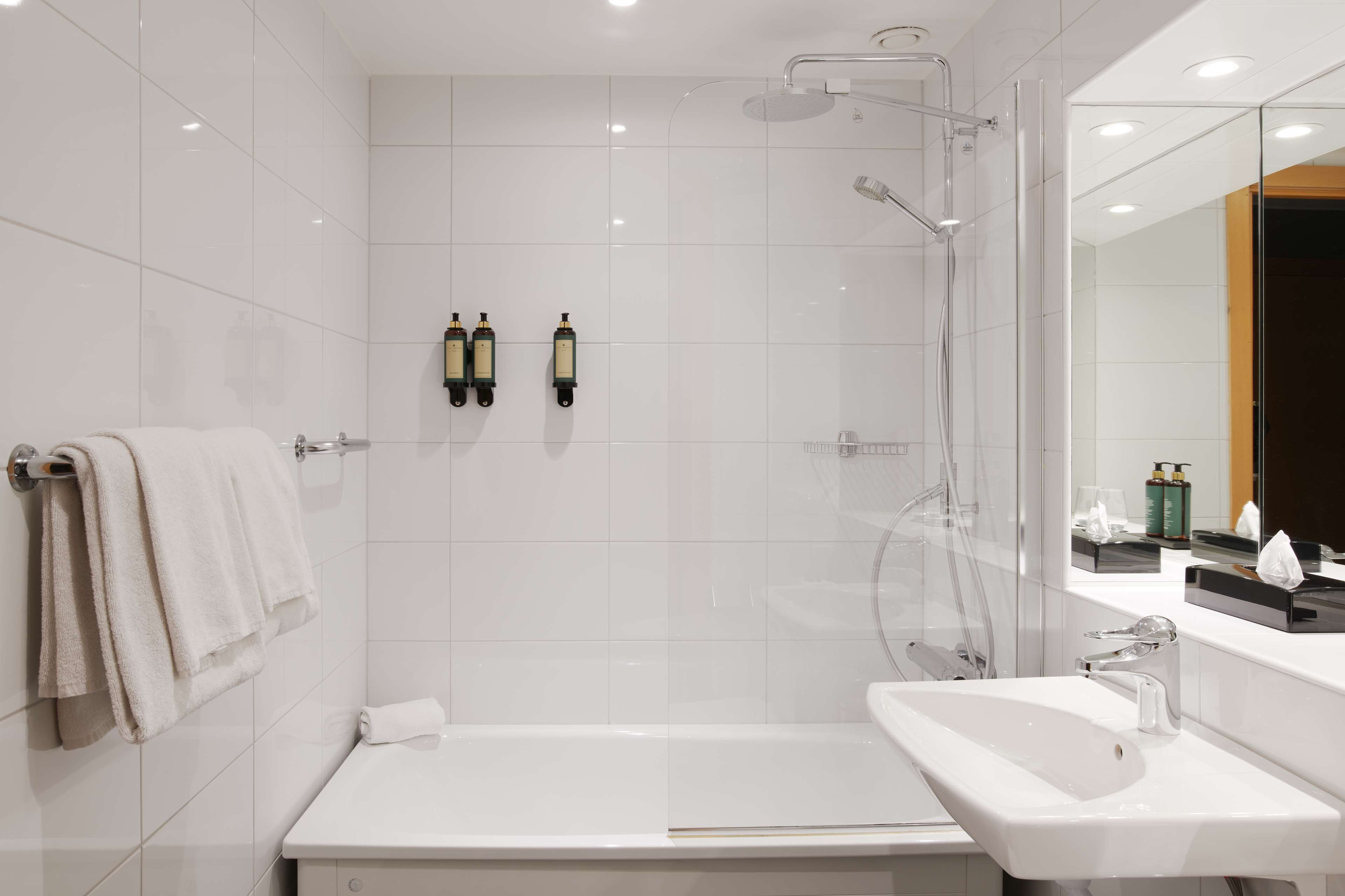 A modern bathroom with a glass-enclosed shower, a white bathtub, and a sink with a mirror above it.