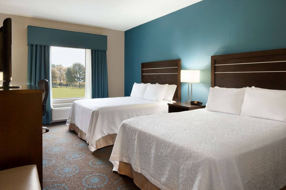 A hotel room with two beds, a desk, a chair, a TV, and a window with curtains.