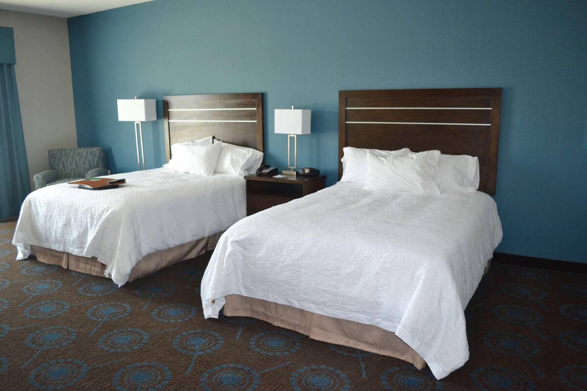 A hotel room with two beds, a nightstand with a lamp, a chair, and a patterned carpet.
