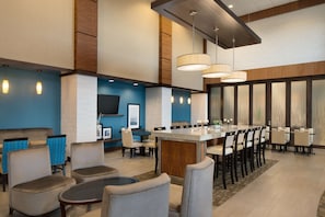 A modern hotel lobby with a long dining table, several chairs, and a bar area.