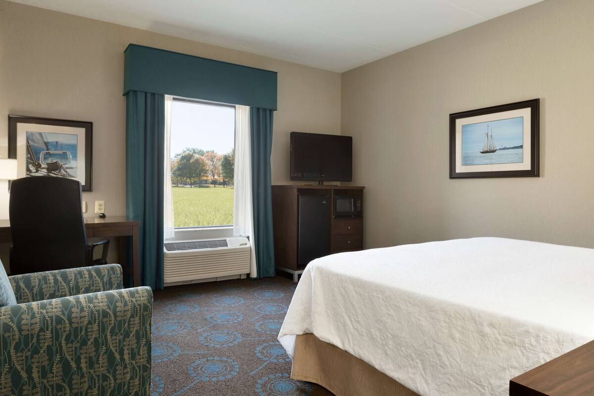 A hotel room with a bed, a desk, a chair, a television, and a window with curtains.