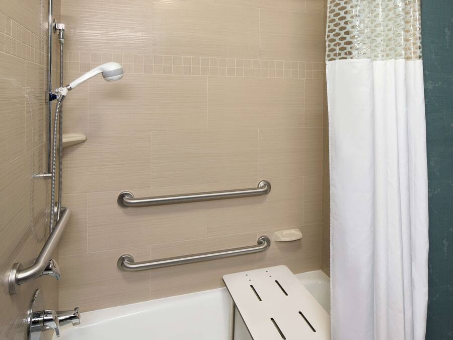 Un baño con bañera, barras de apoyo, ducha y cortina blanca.